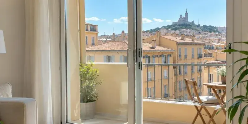Porte-fenêtre coulissante blanche ouverte sur un balcon dominant les toits de Marseille
