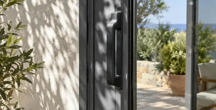 Détail du montant d'une baie vitrée coulissante en aluminium avec sa poignée, ombre de feuillage