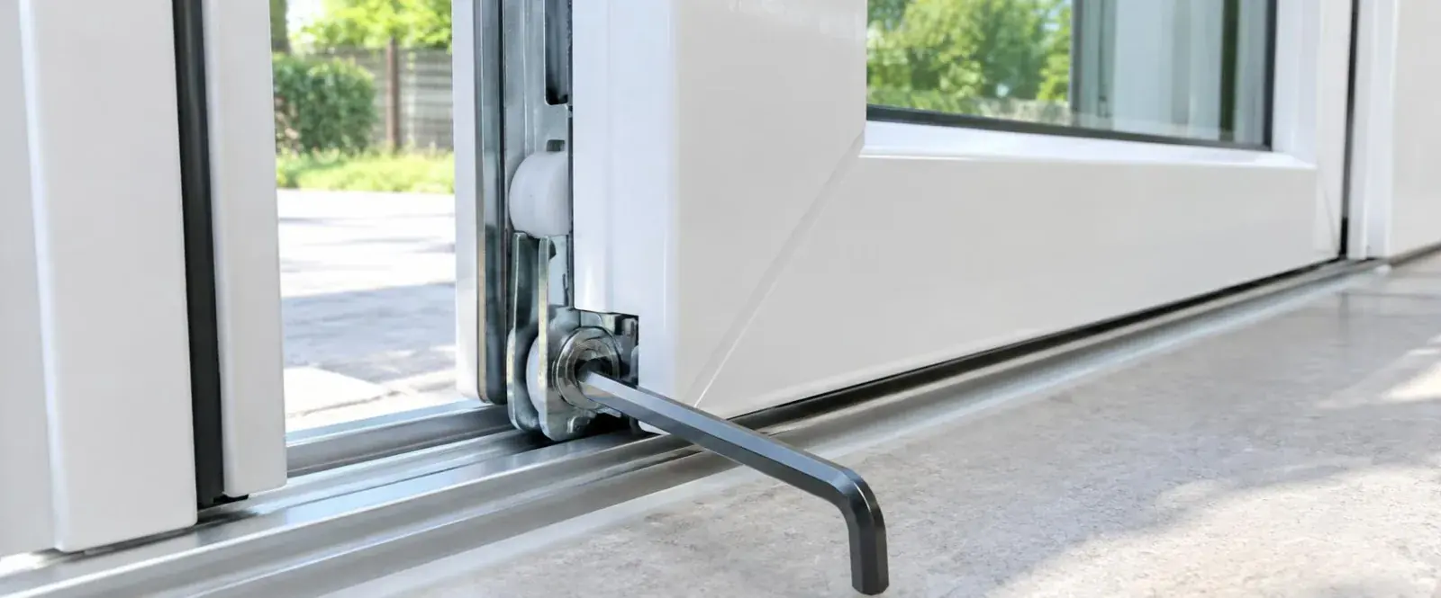 Ferrure et roulette de réglage au bas d'une porte-fenêtre coulissante PVC blanche, clé six pans engagée